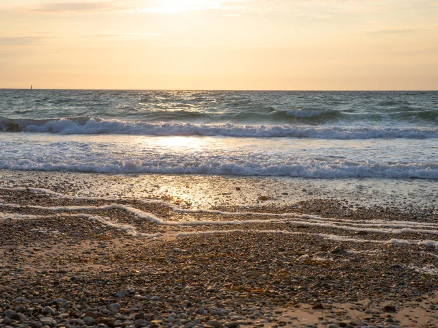 Coucher de soleil sur une plage de galets avec des vagues douces et un ciel doré.