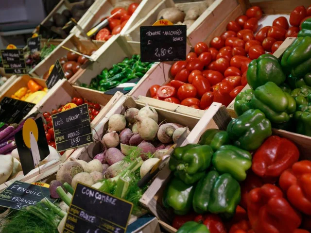 Un étal de légumes frais dans un marché, avec des poivrons, des tomates et des oignons.