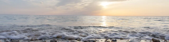 Plage avec des galets et des vagues sous un ciel au coucher du soleil.