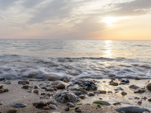 Plage avec des galets et des vagues sous un ciel au coucher du soleil.