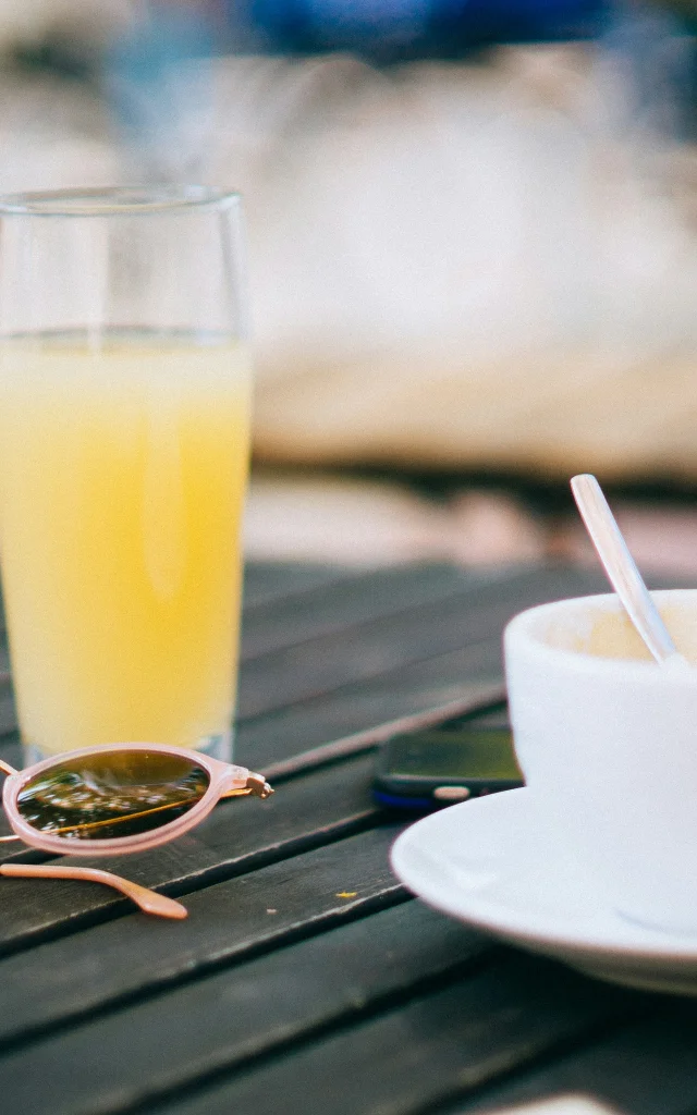 Une tasse de café et un verre de jus d'orange posés sur une table avec des lunettes de soleil.