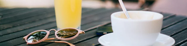 Une tasse de café et un verre de jus d'orange posés sur une table avec des lunettes de soleil.