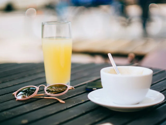 Une tasse de café et un verre de jus d'orange posés sur une table avec des lunettes de soleil.