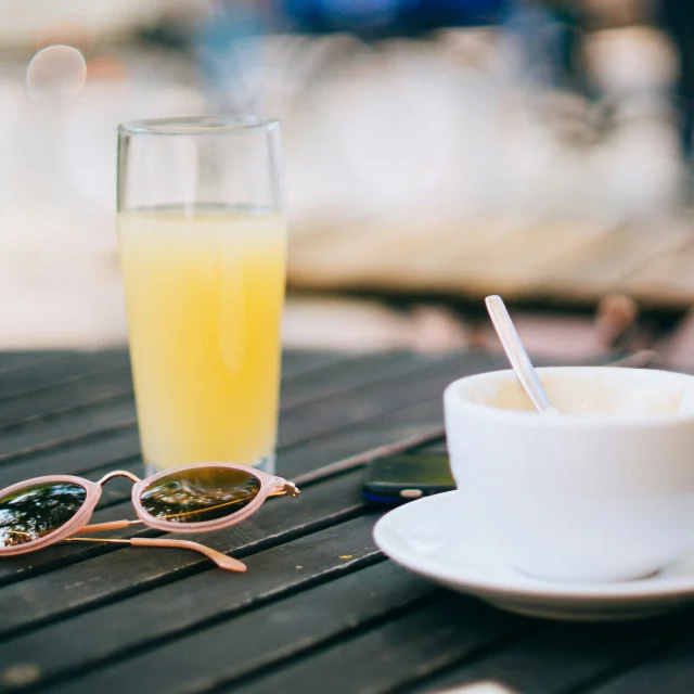 Une tasse de café et un verre de jus d'orange posés sur une table avec des lunettes de soleil.