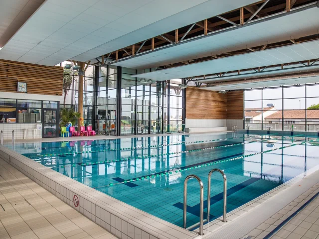 Vue du bassin sportif d'AquaRé avec des chaises colorées et un toit vitré.